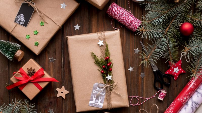 gifts wrapped in brown paper,surrounded by branches of a Christmas tree with red ornaments